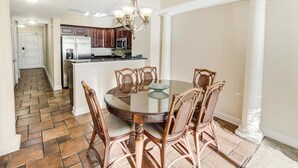 Un coin repas avec une table ronde et six chaises, une cuisine en arrière-plan et un parquet à motifs en chevrons.