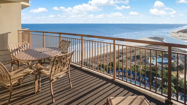 Un balcon avec une table et des chaises en bois, donnant sur une plage et l’océan.