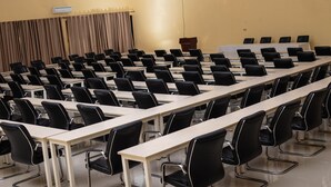 Un salón de conferencias con filas de mesas y sillas, un atril y un telón de fondo.