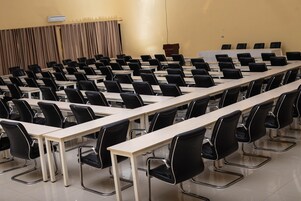 Un salón de conferencias con filas de mesas y sillas, un atril y un telón de fondo.