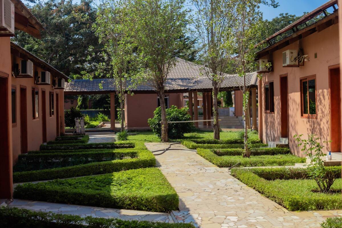 A courtyard with a stone pathway, neatly trimmed hedges, and traditional architecture.
