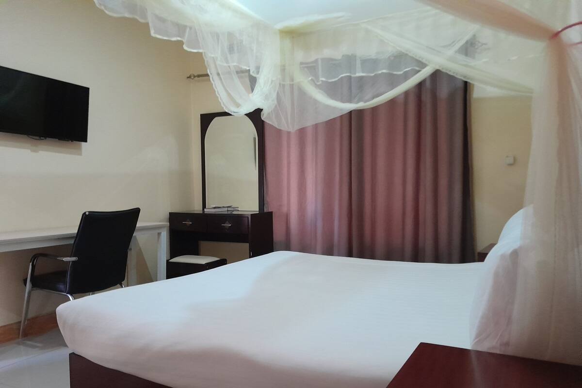 A hotel room with a bed, a desk, a chair, a mirror, and a TV.