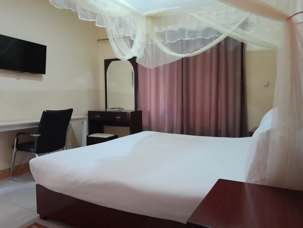 A hotel room with a bed, a desk, a chair, a mirror, and a TV.
