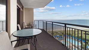 A balcony with a glass table and chairs, overlooking a pool and ocean view.