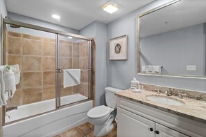 Ein Badezimmer mit einer Duschkabine, einer Toilette, einem Waschbecken mit Marmorplatte und einem großen Spiegel.