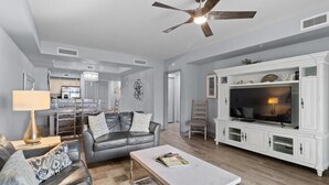A spacious living room with a grey leather sofa, a white coffee table, and a large TV cabinet.