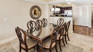 A dining area with a glass-top table surrounded by ornate chairs, a decorative mirror, and a kitchen in the background. - Paradise Found: Oceanfront 3-Bedroom Condo (North Myrtle Beach)