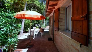 Een terras met een tafel, stoelen, een parasol en een bakstenen gebouw met houten luiken.