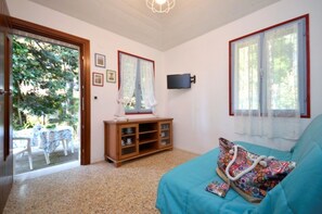 A bedroom with a bed, a TV, a window with curtains, a wooden cabinet, and a door leading to a patio.