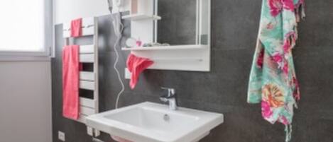 A modern bathroom with a white sink, dark tiled walls, and a red towel on the floor.