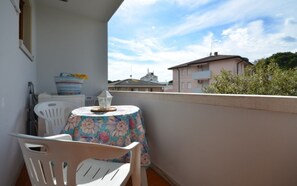 A balcony with a table and chairs, a small lantern, and a view of buildings and trees.