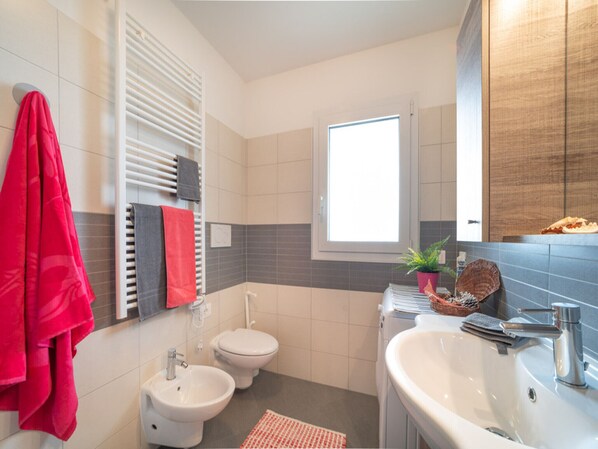 Un baño moderno con bidé, inodoro, lavamanos y ventana que proporciona luz natural.