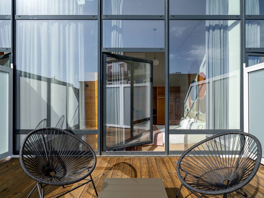 Un interior moderno con grandes ventanas de vidrio, dos sillas de alambre negras y piso de madera.