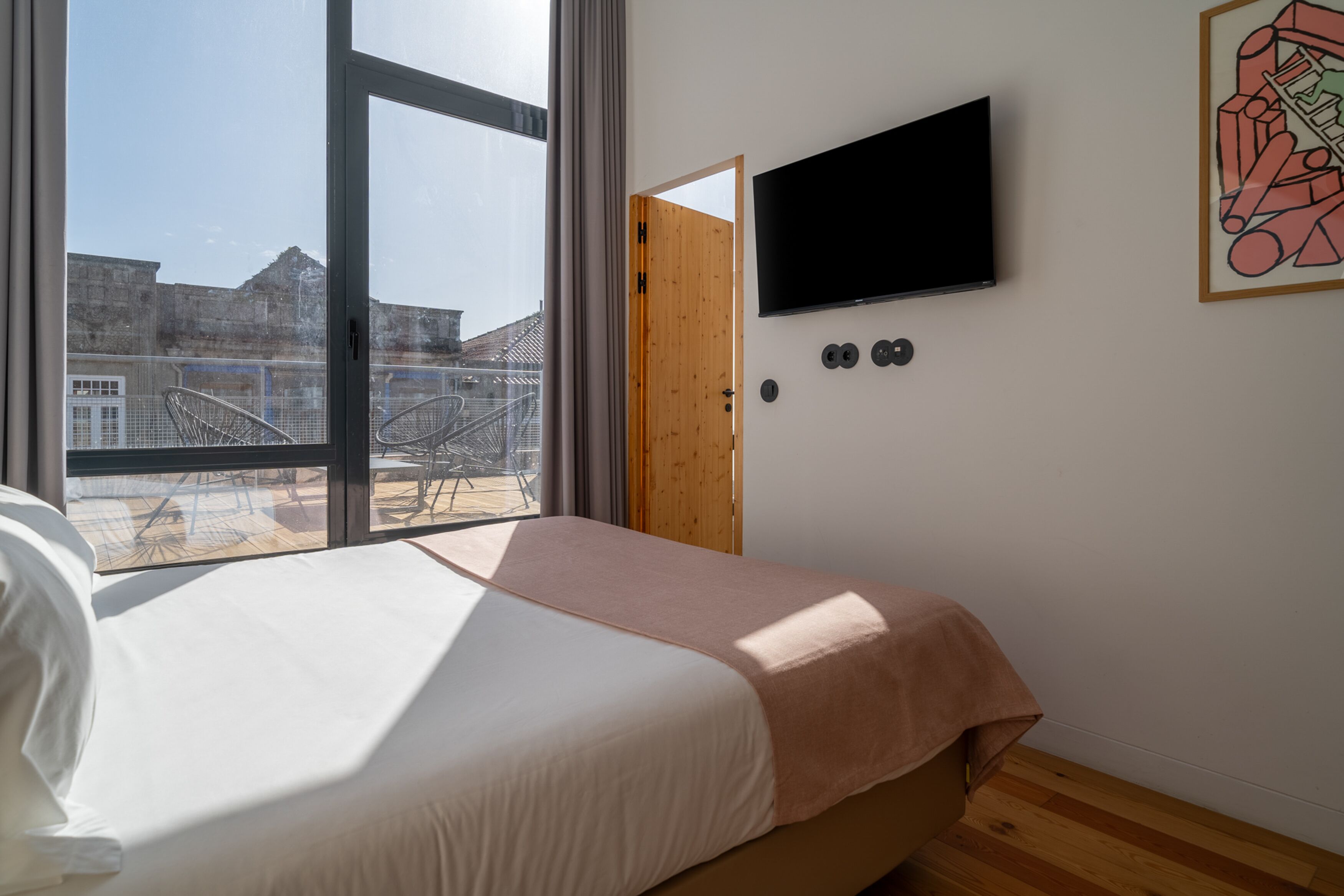 A bedroom with a bed, a TV, and a window with a view of buildings.