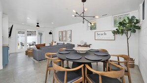 A modern living room with a grey sofa, a dining table with wooden chairs, and a ceiling light fixture.