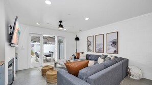 A modern living room with a grey sectional sofa, a flat-screen TV mounted on the wall, and a ceiling fan.