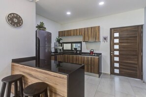 Kitchen features a central island with a countertop, cabinetry, refrigerator, microwave, and kettle.