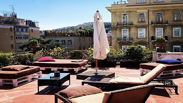 A rooftop terrace with lounge chairs, a table, and an umbrella.
