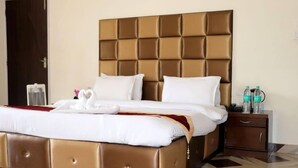 A hotel room with a large bed, a wooden nightstand, and a water bottle on the nightstand. - Snow Touch Resort By Sriniwasa Hotels (Kullu)
