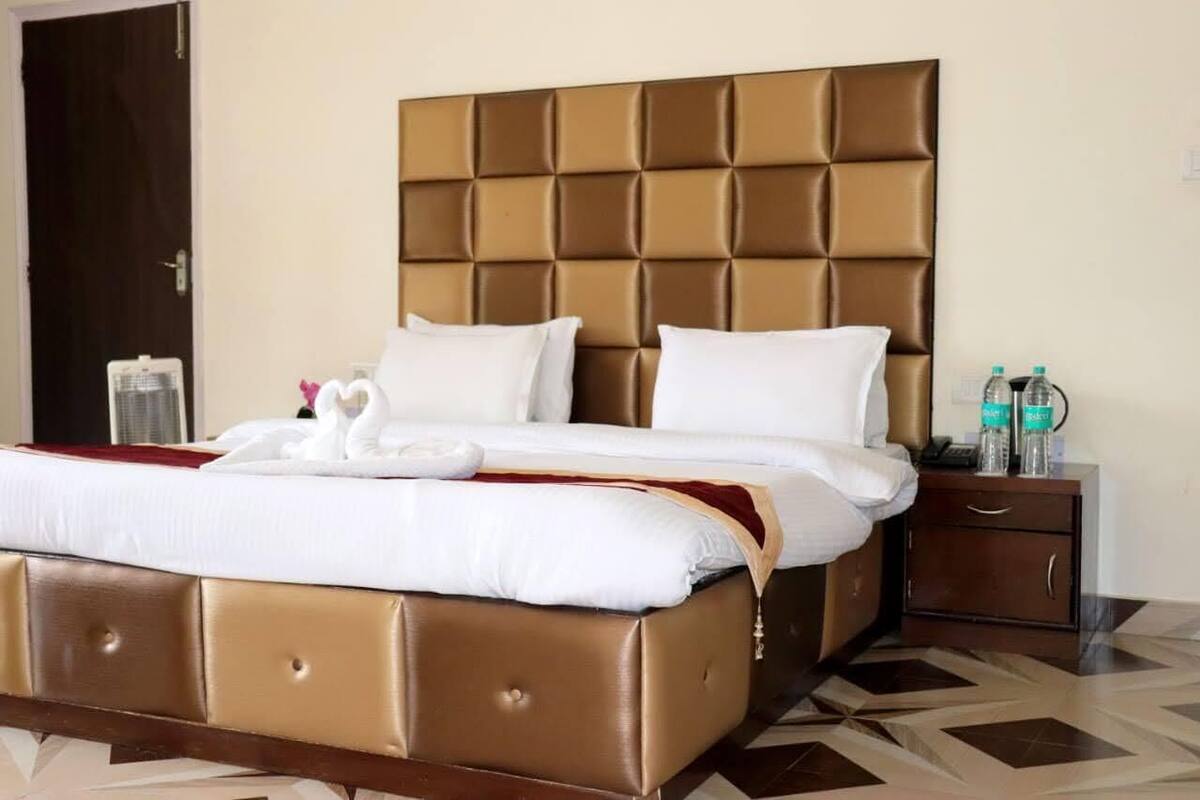 A hotel room with a large bed, a wooden nightstand, and a water bottle on the nightstand.