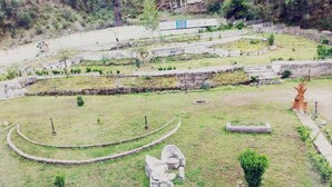 A landscaped area with stone sculptures, a fenced perimeter, and a building in the background. - Snow Touch Resort By Sriniwasa Hotels (Kullu)