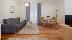 Un salon comprenant un canapé, une table à manger avec des chaises, un téléviseur et une fenêtre avec des rideaux.