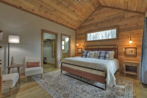 Une chambre confortable avec un grand lit, une petite chaise, une table de chevet et une fenêtre.