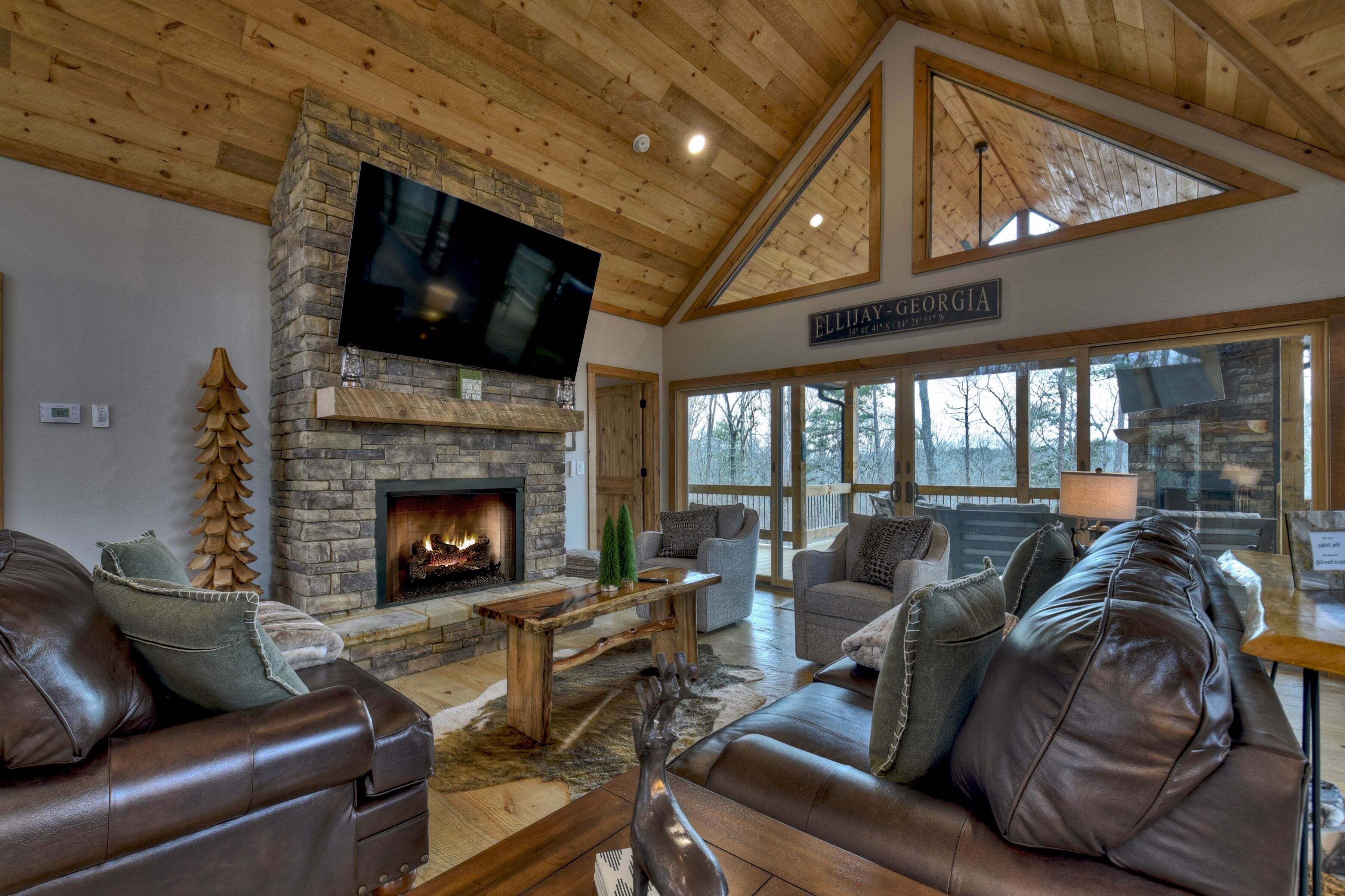 A cozy living room with a stone fireplace, leather sofas, and a large TV mounted on the wall.