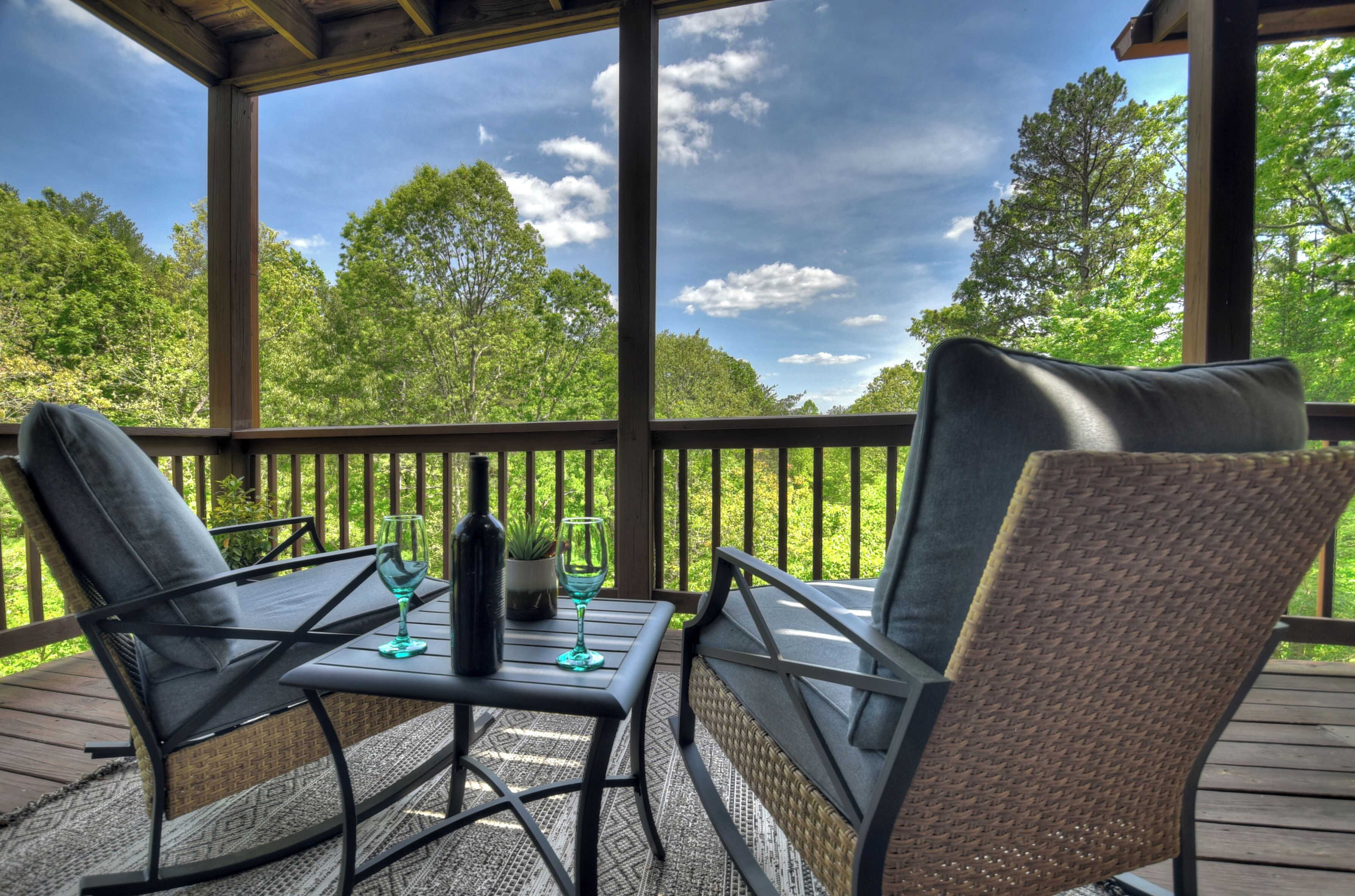 A covered outdoor seating area with two chairs and a table, a bottle, and a glass on the table.