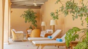 Un salon lumineux, meublé de meubles en osier, doté d’un ventilateur de plafond et agrémenté de plantes en pot.