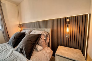 A modern bedroom with a bed, bedside table, and wall-mounted light fixtures.