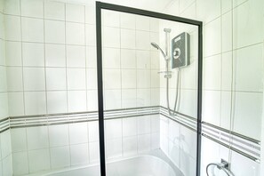Glastrukket brusebad med håndbruser, vandhane på væggen og flisegulv.