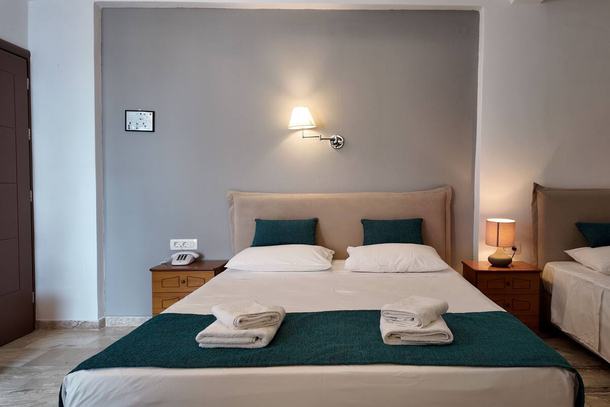 A hotel room with two beds, each with a headboard, a bedside table with a lamp, and a folded towel on the bed.