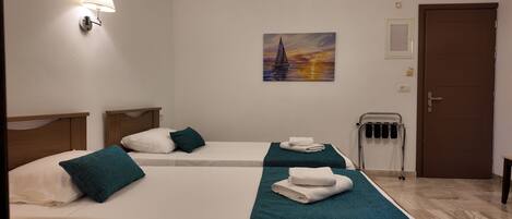 Una habitación de hotel con dos camas, cada una con una manta color turquesa y almohadas blancas, un cuadro de un velero en la pared, un perchero y una puerta.