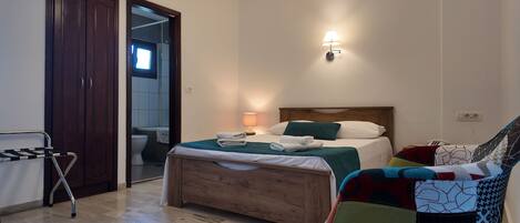 A bedroom with a wooden bed, a bedside table with a lamp, a chair with a colorful blanket, and a wooden wardrobe.