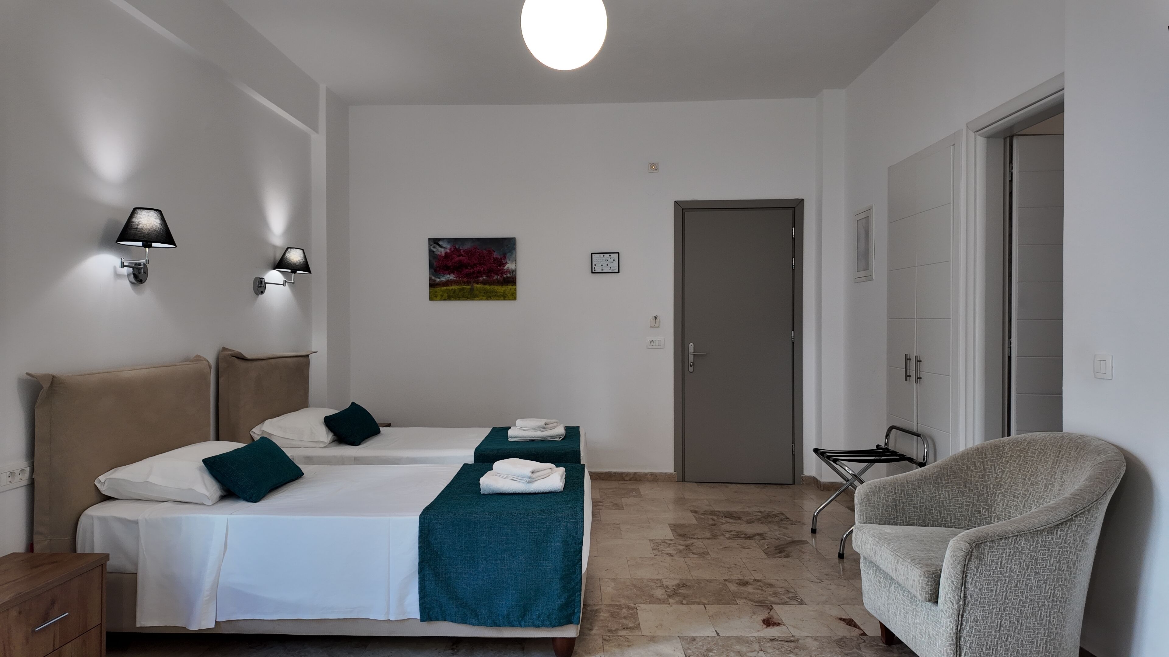 Habitación de hotel con dos camas, una silla, un cuadro y una puerta.