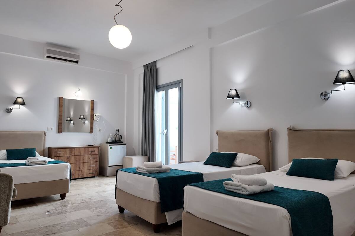 A hotel room with two beds, a desk, a chair, a mirror, and a window.