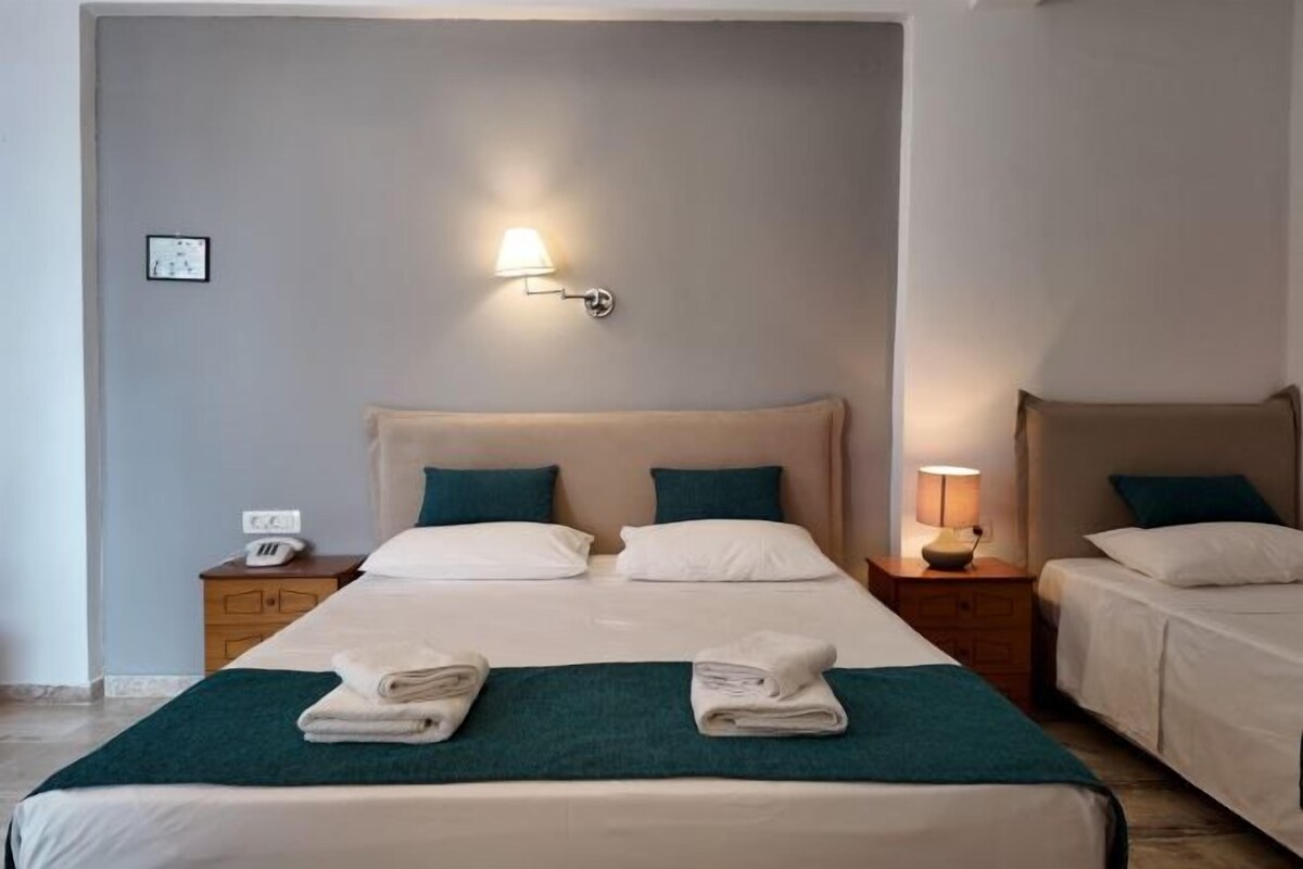A hotel room with a large bed, two bedside tables, a wall-mounted lamp, and a small bedside table with a lamp.