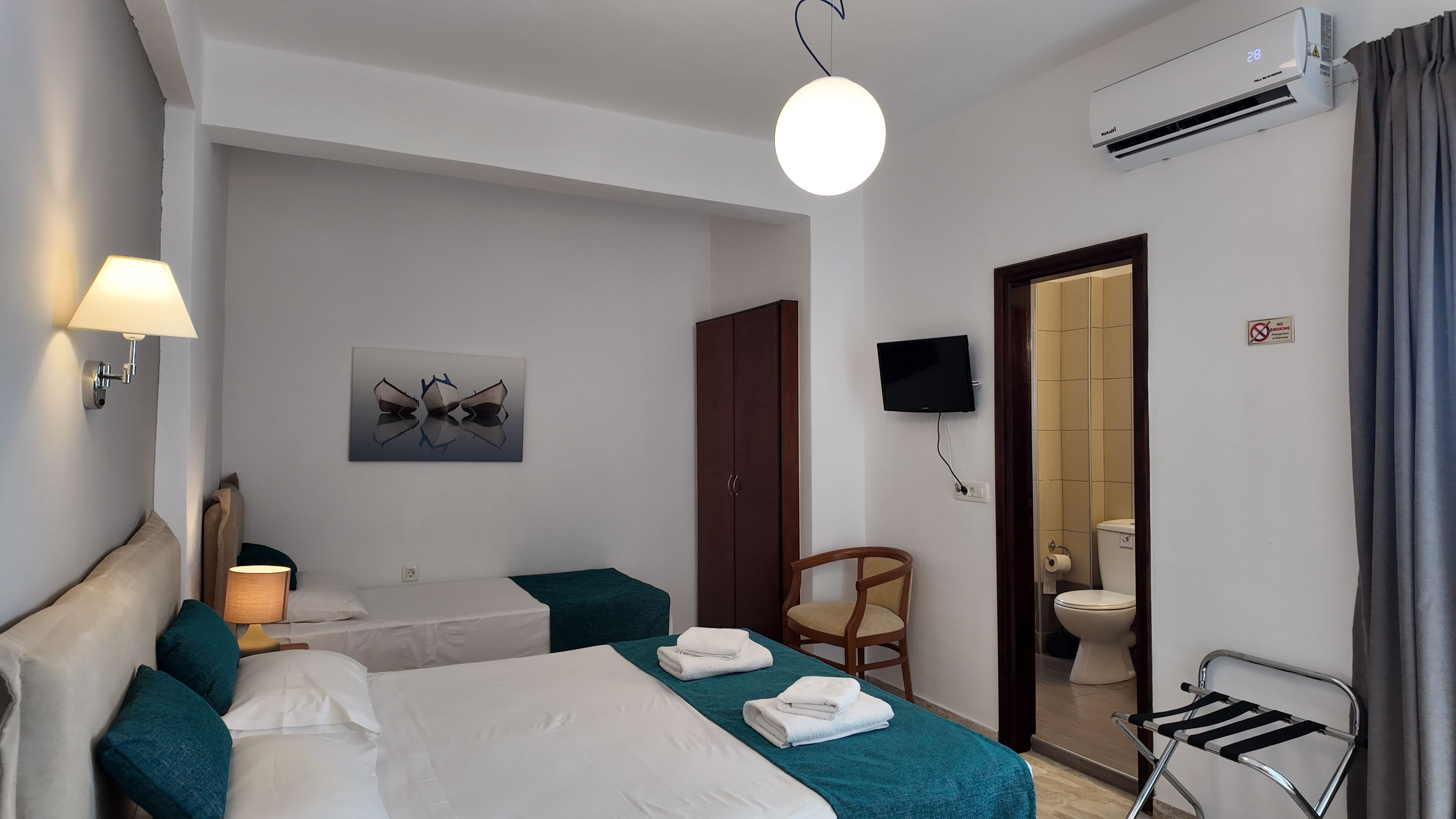 Habitación de hotel con dos camas, televisión, aire acondicionado, un cuadro y un baño visible a través de una puerta abierta.