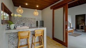 A modern kitchen with a marble countertop, two wicker bar stools, a refrigerator, and a hanging light fixture. - Suarga Loka Ubud Villa (Ubud)