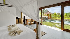 A bedroom with a large bed, a desk, and a view of a swimming pool and garden. - Suarga Loka Ubud Villa (Ubud)