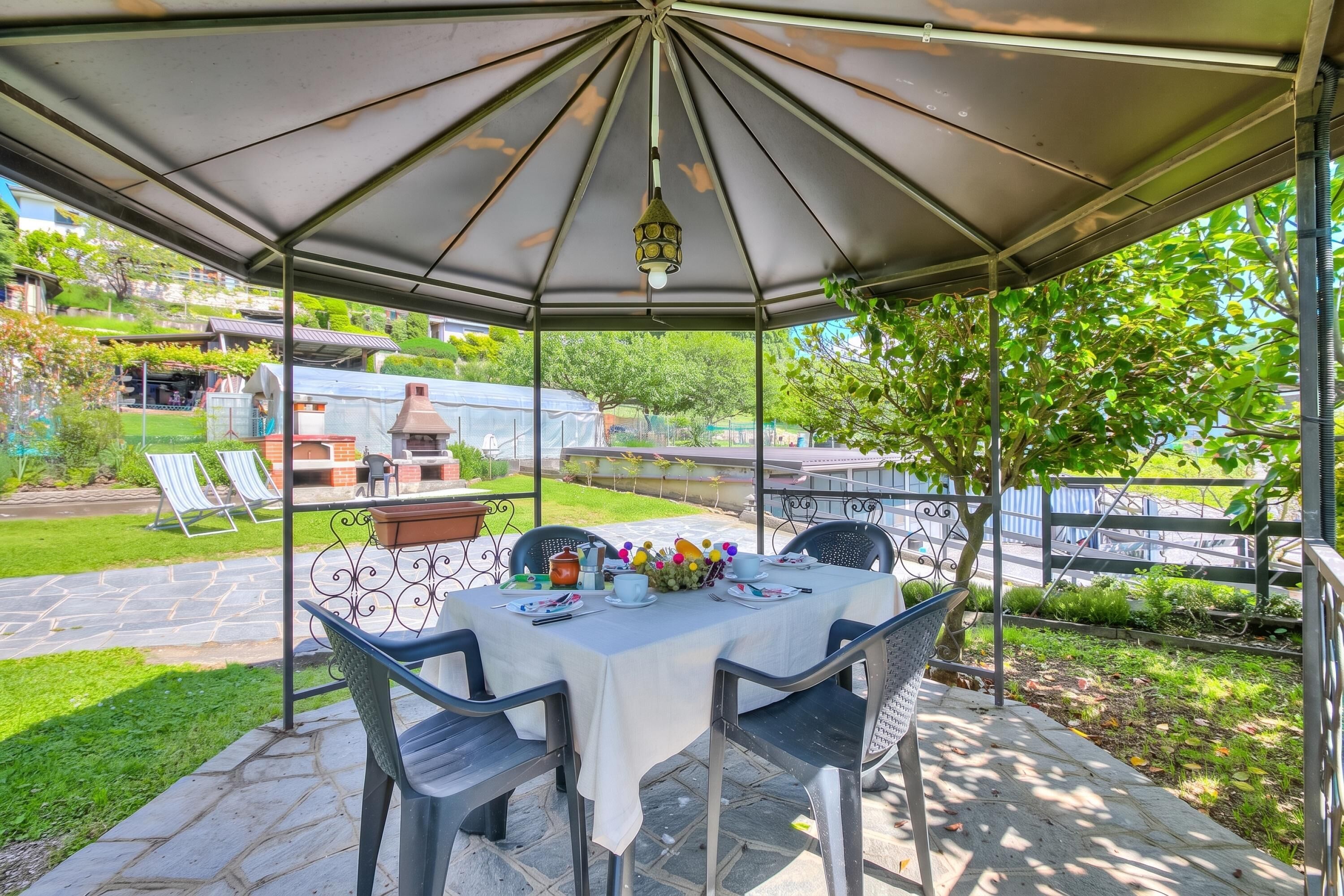 A covered patio with a table set for dining, surrounded by chairs, and a hanging light fixture.