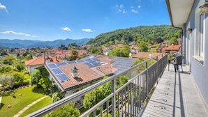 A balcony with a view of a residential area, solar panels on a house roof, and a mountainous landscape.