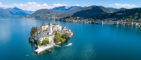 A lakeside property with a prominent building surrounded by water, boats, and a mountainous backdrop.