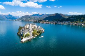 Una isla con un edificio grande rodeado de agua, barcos y montañas al fondo.