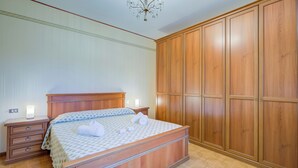 A bedroom with a large bed, wooden wardrobe, and a chandelier.