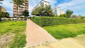 A pathway leading to a residential building with multiple floors, surrounded by well-maintained grass and trees. - A1040 - First line of the sea in El Torres beach (Villajoyosa)