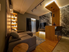 A modern living room with a sofa, a coffee table, a TV, and a stone wall. - Night Pearl - Deluxe Apartment (Bar)
