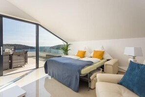 Quarto moderno com cama, sofá, escrivaninha e uma grande janela com vista panorâmica.