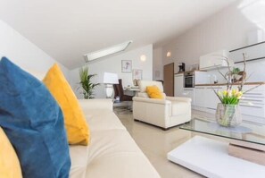 Ein modernes Wohnzimmer mit einer Couch, einem Glastisch und einer Küchenzeile im Hintergrund.